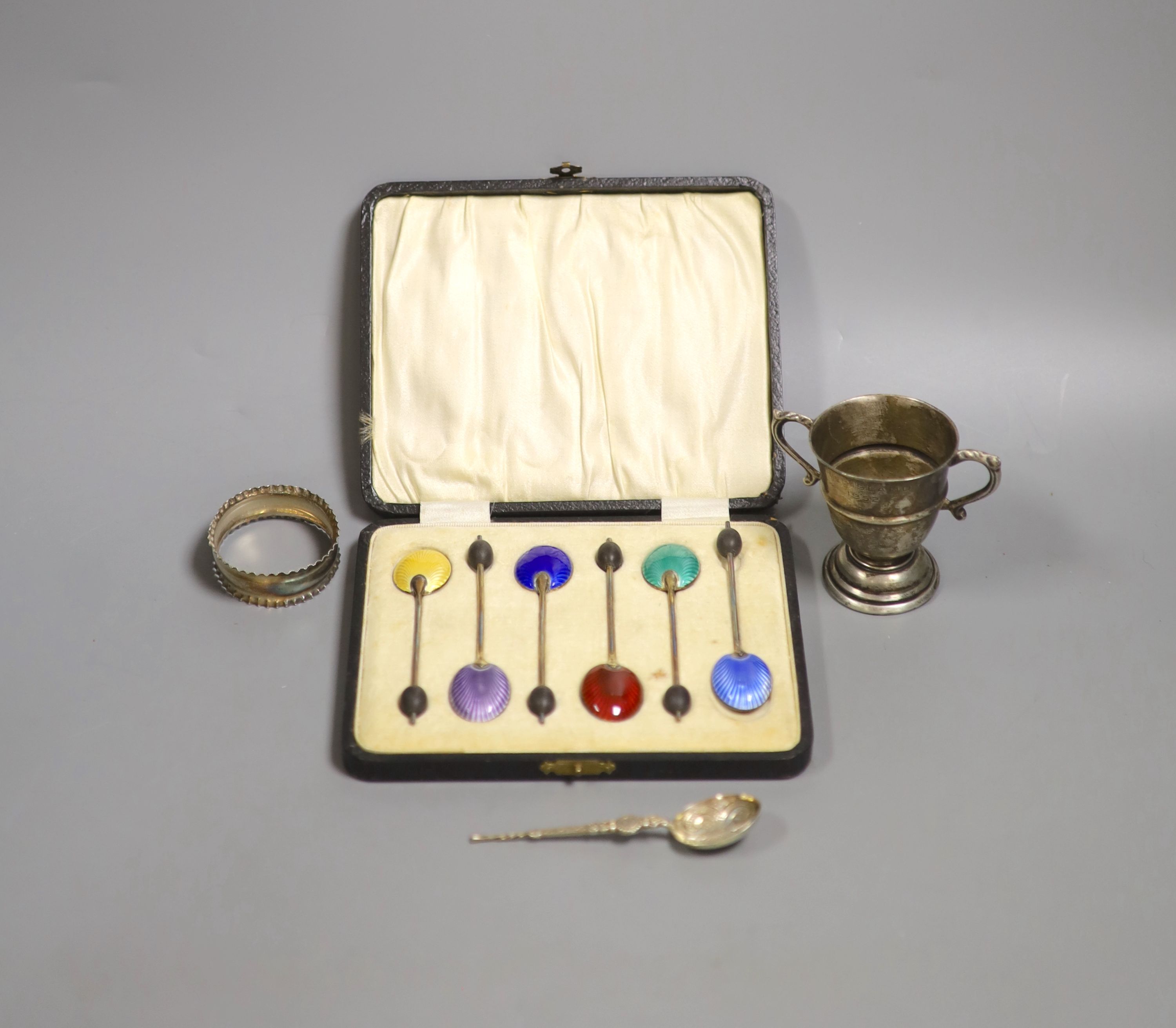 A cased set of six silver and enamel(a.f.) bean end coffee spoons, one other silver spoon, a silver napkin ring and small silver trophy cup.